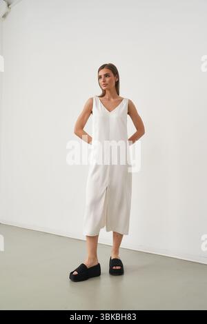 Woman in a sleeveless white dress and black platform shoes poses confidently. Her hands rest behind her back, and her gaze is forward. Minimalist Stock Photo