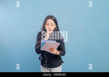 A woman is reading a book while looking at the camera. She is surprised or shocked by something she is reading Stock Photo