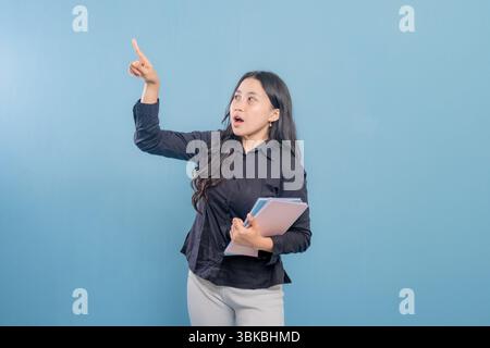 A woman is pointing at something while holding a stack of books. Concept of importance and focus, as the woman is likely trying to convey a message or Stock Photo