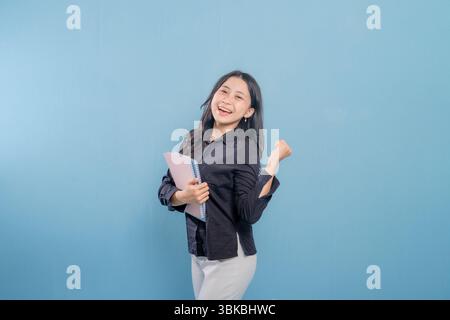 A woman is holding a book and smiling. She is happy and excited. Concept of joy and enthusiasm Stock Photo