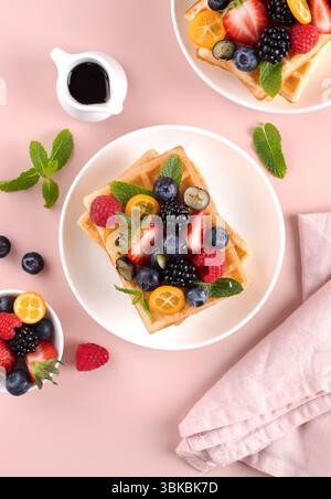 Crispy Belgian waffles with fresh berries and maple syrup on pink background. Top view. Stock Photo
