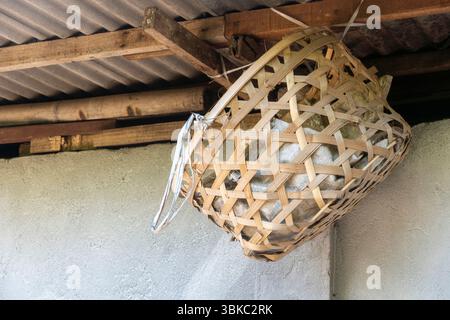 Basket hanging from a rafter with a white object inside. The basket is made of wood and has a woven design Stock Photo