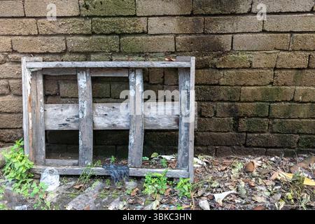 Wooden crate is sitting on the ground next to a brick wall. The crate is covered in dirt and has a few pieces of trash on it. Scene is one of neglect Stock Photo