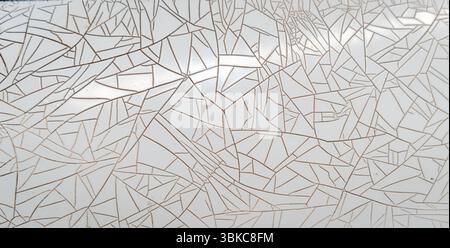 A close-up view of a deteriorating white plastic sheet featuring a complex network of cracks and peeling patterns, creating an abstract geometric desi Stock Photo