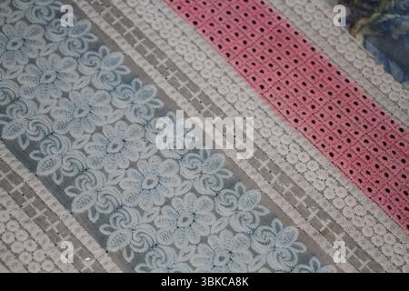 A beautifully patterned textile featuring alternating stripes of lace and embroidery. The design includes detailed floral motifs in light blue. Stock Photo