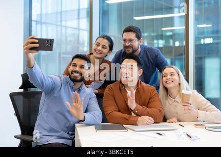 A diverse group of colleagues taking a selfie together in a modern office setting, showcasing teamwork and collaboration. Stock Photo
