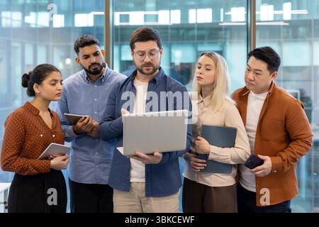 A diverse group of business professionals collaborates in an office setting, examining a laptop screen intently during a meeting. Stock Photo