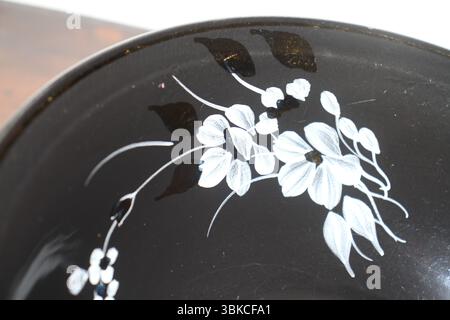 A close-up of a decorative floral design painted in white on a glossy black ceramic surface, the part of a bowl. Stock Photo