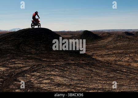 A young man rides his dirt bike up and over a hill while motocross riding the surreal dunes near Cameron, AZ. Stock Photo