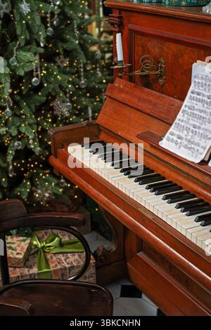 Holiday decorated piano with sheet music and shining Christmas tree. Stock Photo