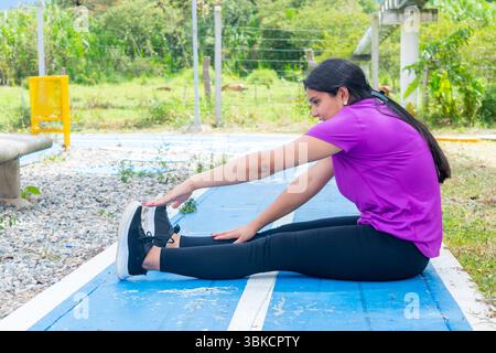 Young Latina Woman Stretching Hamstrings Outdoors on Track Stock Photo