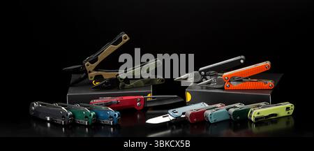 Multitools with colorful handles displayed on a reflective black surface, showing open and closed configurations Stock Photo