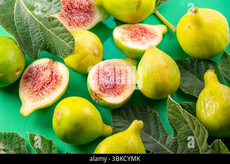 Ripe green fig fruits with fig leaves and fig pieces isolated on green background. Stock Photo