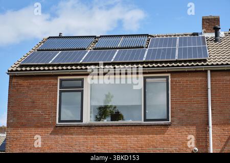 Netherlands: Older row house with solar panels and solar heat pipes installed side by side on a gray concrete tiled roof in the Dutch village of Ooste Stock Photo