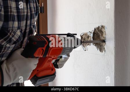 Carpenter electrician with demolition hammer prepares the cavity in the wall where to insert the built-in electrical panel. Work safely with protectiv Stock Photo
