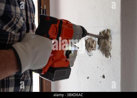 Carpenter electrician with demolition hammer prepares the cavity in the wall where to insert the built-in electrical panel. Work safely with protectiv Stock Photo