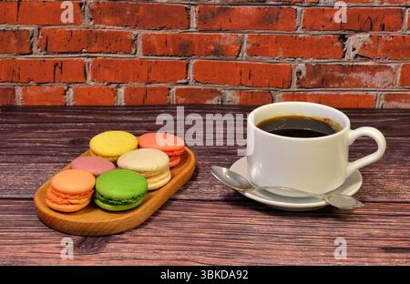 Cup of black coffee and wooden plate with several colorful macaroons on wooden table. Close-up. Stock Photo