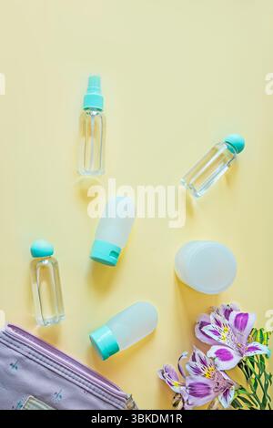 Arrangement of toiletry containers and a small floral pouch with purple alstroemeria on soft yellow background. Clean, organized and elegant travel es Stock Photo