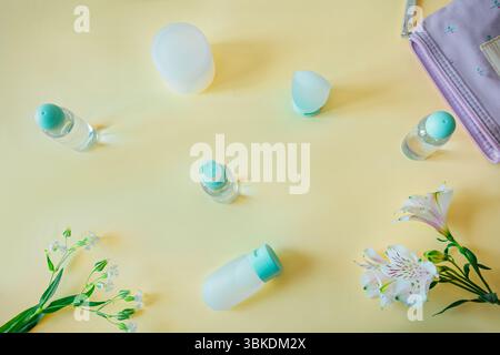 Flat lay arrangement of skincare bottles and flowers on pastel yellow background. Balanced layout with soft natural light, perfect for vacation, beaut Stock Photo