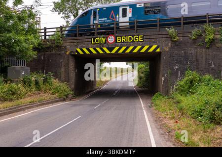 Passenger train gliding over a low bridge on a tranquil country road in the picturesque landscapes of the United Kingdom Stock Photo