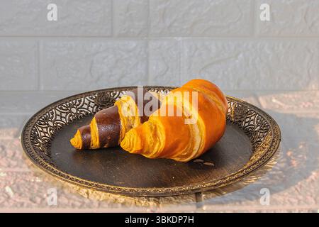 Freshly baked golden and chocolate croissants served on a round ornamental black plate. Perfect for breakfast presentation, bakery menu, or food photo Stock Photo