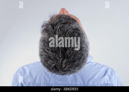 A man with a balding head and gray hair. He is wearing a blue shirt. The man is looking up at the camera Stock Photo