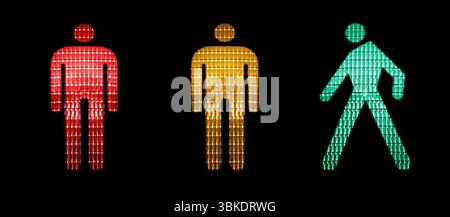 Red, yellow and green figures of a pedestrian traffic light isolated on black background. Stock Photo