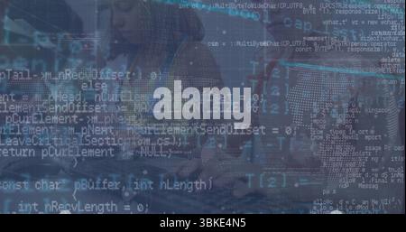 Developer in hoodie typing at laptop beside coworker in office, with coding overlay and world map Stock Photo