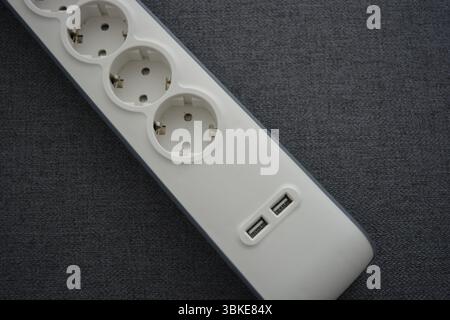 Things, electrical items. New stylish outlet, white stylish extension cords with powerful gray wire, two USB connectors are located on a gray fabric. Stock Photo