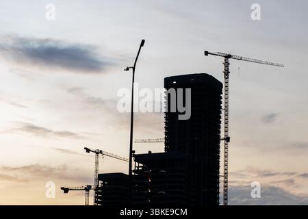 At a bustling construction site, various cranes are towering over the area where a highrise building is currently under construction Stock Photo