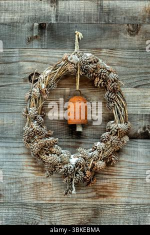 A wreath made of pinecones and natural materials is displayed on a rustic wooden wall. An antique bell adds a charming touch, Aubrac, Occitanie.France Stock Photo