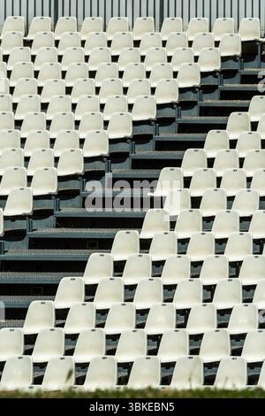 Empty white seats neatly arranged in rows await spectators at a stadium. Stock Photo