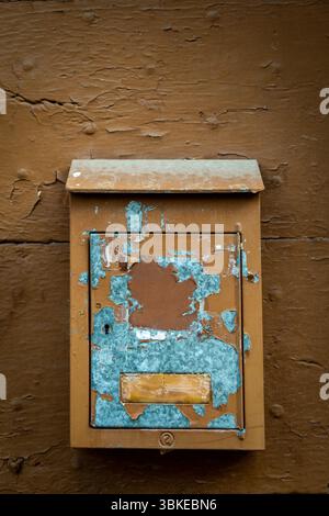 A rustic mailbox is mounted on a weathered brown wall, featuring peeling paint and faded colors. Auvergne. France Stock Photo