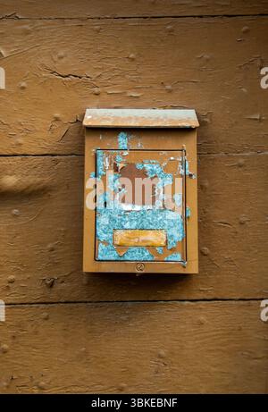 A weathered mailbox hangs on a rustic wooden wall, showcasing chipped paint in blue and brown tones.  Auvergne. France Stock Photo