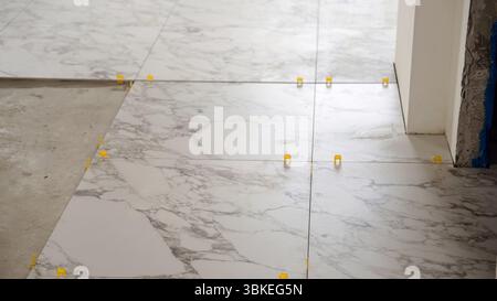 Professional tiler carefully positioning oversized marble tiles on floor, utilizing precision tile spacers and leveling system for seamless, high-qual Stock Photo