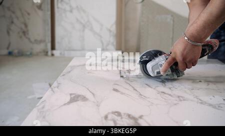 Tiler cutting tiles with angle grinder. The master cuts large ceramic tiles. Stock Photo