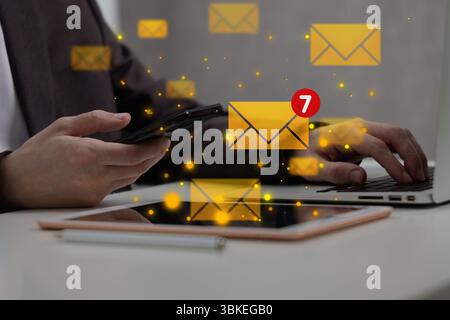 Email marketing, new message notification. Man using laptop and mobile phone at table, closeup Stock Photo