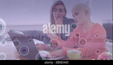 Collaborating two women working in living room workspace with 5G network overlay, laptop and mug Stock Photo