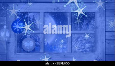 Displaying window with frost in cabin, hanging blue snowflake baubles before moonlit pine forest Stock Photo