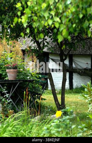 Idyllic garden scene with a table and chair in front of a traditional thatched-roof house in summer. Stock Photo