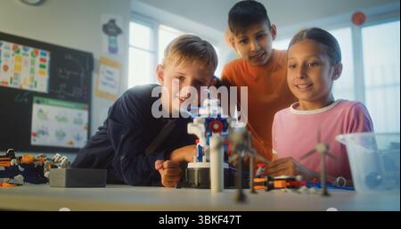 Happy Elementary School Students Studying Model of Robotic Arm Together. Group of Kids Sitting at Table During Science and Engineering Lesson in Multicultural Classroom. Interactive STEM Education. Stock Photo
