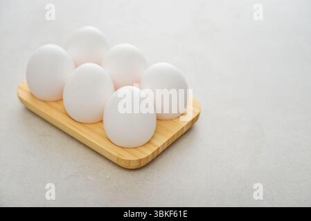 Eggs with white shell in wooden egg holder on light background closeup Stock Photo