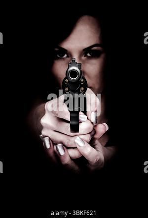 A woman is holding a gun, pointing it directly at the viewer. The woman's eyes are visible in the background, and the gun is the main focus of the ima Stock Photo