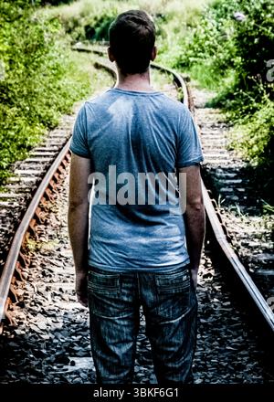 A man standing on train tracks, viewed from the back. Stock Photo