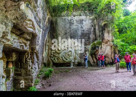 The Lapidiales sculptures in Port-d'Envaux, Nouvelle-Aquitaine, France, cover the rock faces of a former quarry. In the centre, a large relief shows a swirling form with figures, and on the left, figures sit in niches in the wall. Six visitors (possibly participants in the guided cycling tour by Die Landpartie) look at and photograph the reliefs. Various artists have carved the Lapidiales into the rock. The works depict different figures and scenes. The works of art are part of the landscape and blend harmoniously into the natural surroundings. They are an example of the art and history of the Stock Photo