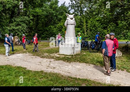 Group of cyclists at the land art project 'La Galaxie des Pierres Levées', here at a work by Aldo Shiroma Uza from Peru with the work 'KItsune comtemplatif'. The Lapidales sculptures are carved into the rock of a former quarry by various artists and depict different figures and scenes. The works of art are part of the landscape and blend harmoniously into the natural surroundings. They are an example of the art and history of the region. Port-d'Envaux, Nouvelle-Aquitaine, France Stock Photo