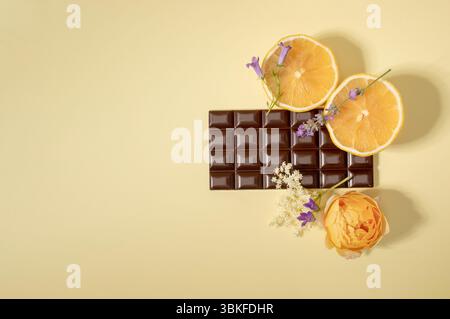 Creative composition made of dark chocolate, lemon and yellow flower against beige background. Flat lay, top view, copy space Stock Photo