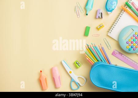 Back to school concept. Flat lay, top view colorful school supplies, blue pencil case, calculator, notepad on light yellow background. Stock Photo