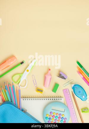 School supplies on a light yellow background. stationery, including pencils, markers, and scissors in a blue case, along with calculator and notebook Stock Photo