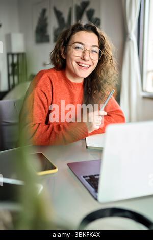 Happy young woman student laughing using laptop sitting at desk studying online. Stock Photo